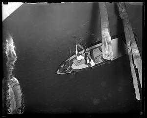 Two men pulling a body out of water from a boat, a policeman beside them