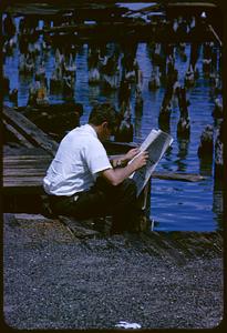 Man reading newspaper next to pier