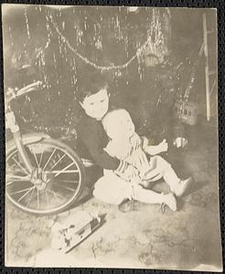 Two toddlers seated under a Christmas tree