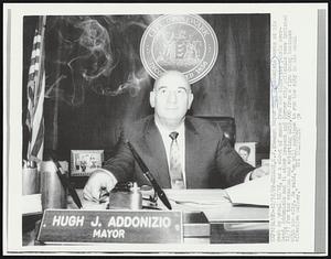 Newark, N. J.: Newark Mayor Hugh J. Addonizio works at his desk as usual 12/18, as a cloud of smoke from his cigarette swirls overhead. Addonizio and 14 other present and former city officials were indicted 12/17 for tax evasion and extorting $253,000 from a firm doing business with the city. He said, "we will continue to run the city in its usual effective manner."