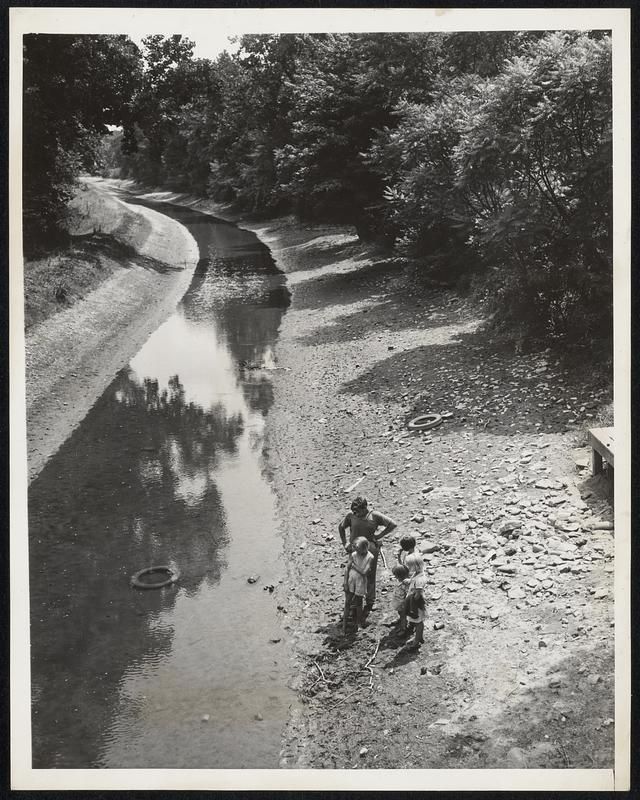 A Scene in Pennsylvania As Drought Becomes More Serious. Yardley, Pa. -- Taken here yesterday is this view of the Lehigh Canal, which is gradually becoming no more than a thin trickle of water because of the continued dry spell. A discarded rubber tire in the center indicates its shallowness to the group of young people standing at a spot where the water formerly ran deep. This is a typical acne in this state where the drought, one of the worst on record, has caused great damage to crops.