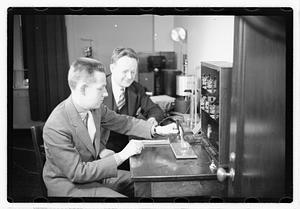 A boy sitting next to a man using an unidentified device