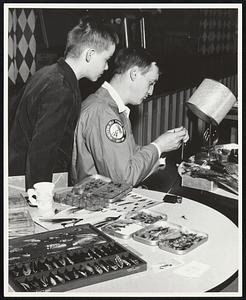 A boy looks over a man's shoulder as he ties a fly