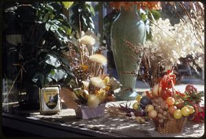 A flower arrangement next to a basket of fruit