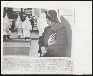 'We Believe in White Supremacy'-- An unidentified Negro woman watches robed Ku Klux Klansmen walking in downtown Montgomery today prior to a cross-burning rally tonight. Circulars advertising the Klan meeting said "We believe in white supremacy. We need you--you need us." Negroes have boycotted city buses here for nearly a year in protest against segregation.