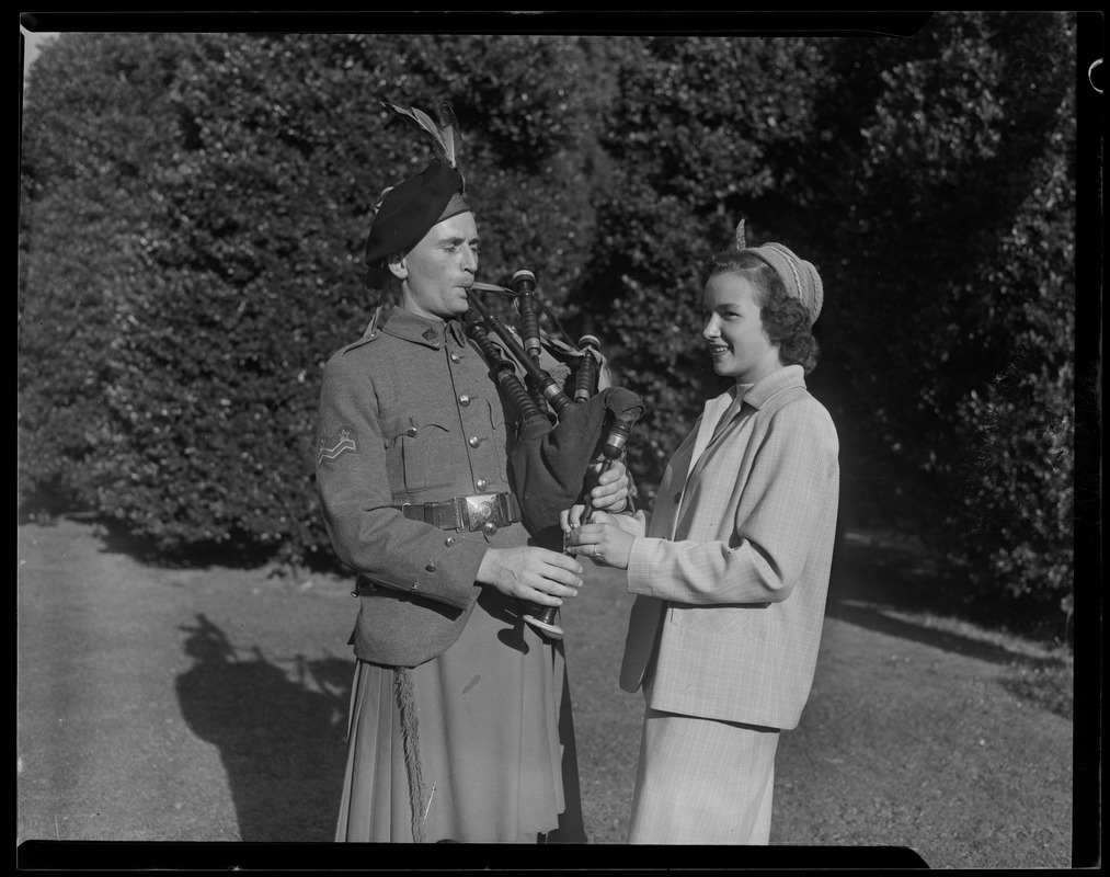 A man stands beside a woman playing the bagpipes