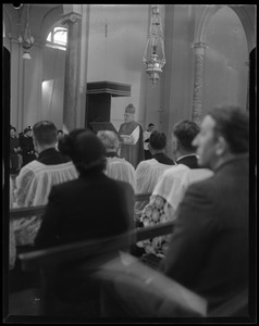 Rev. Cushing stands in a church leading a congregation through a religious ceremony