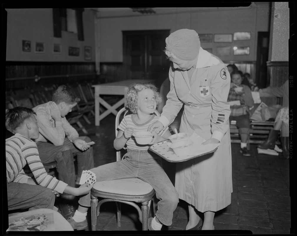 Red Cross worker serving food to children who are playing cards