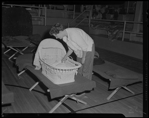 Woman looking at a baby in a basket on a cot at a gymnasium shelter