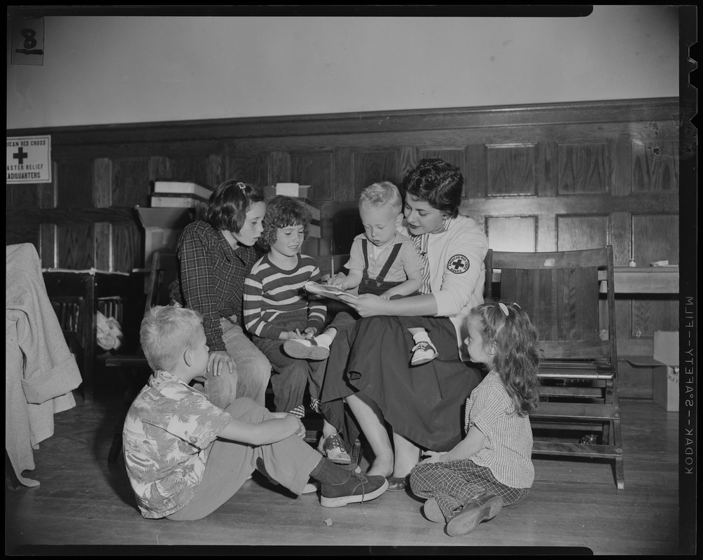 Red Cross volunteer reading to five children, with one in her lap