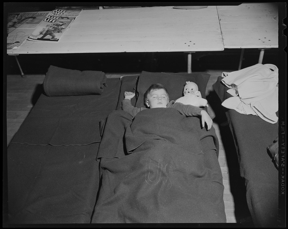 Child with a doll, sleeping on a cot at a shelter