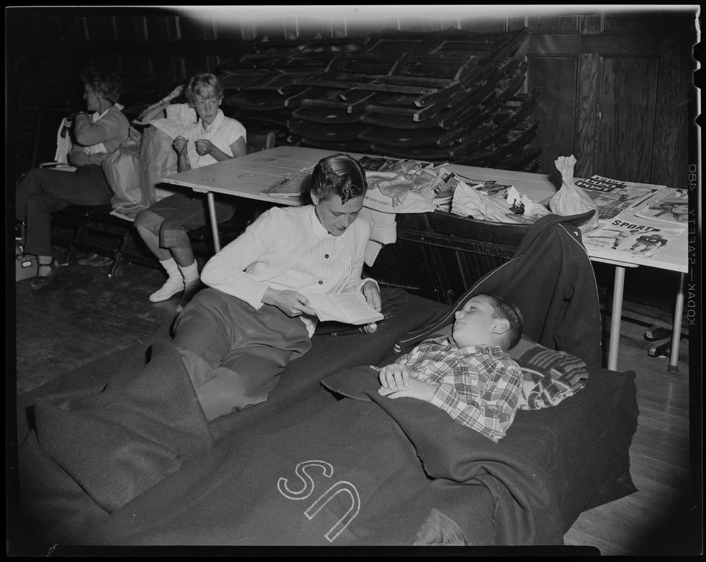 A woman and child rest on cots at a shelter. The woman reads to the child