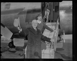 Harry S. Truman standing on airplane stairs, waving a hat before