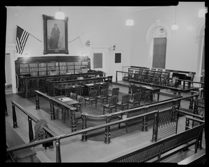 Courtroom interior from the corner, looking at the judge's box with two flags hanging from the wall