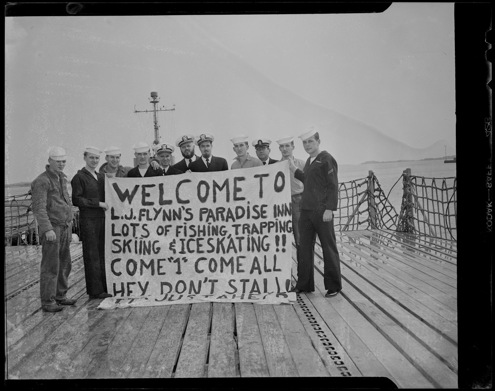 Group photo with banner reading "Welcome to L.J. Flynn's Paradise Inn. Lots of fishing, trapping, skiing and ice skating!! Come '1' come all. Hey don't stall, it's just ahead"