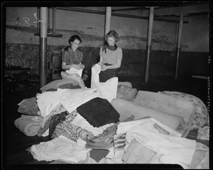 Women standing beside a pile of blankets and mattresses