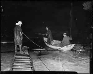 Two men in a boat with a fire fighter standing on ladder beside them