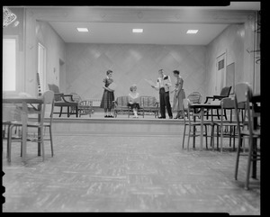 Group of three students and an instructor on a stage with tables and chairs in the foreground