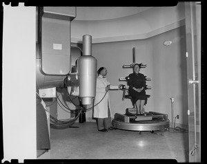 Woman sitting on a piece of hospital equipment while a man stands beside
