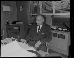 Dr. William H. H. Turville, superintendent of Shattuck Hospital sitting at a desk and holding a piece of paper
