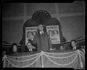 Leverett Saltonstall on stage speaking, in front of campaign posters