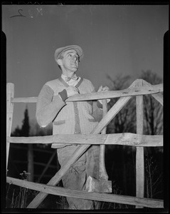 Leverett Saltonstall leaning against a fence, holding an axe