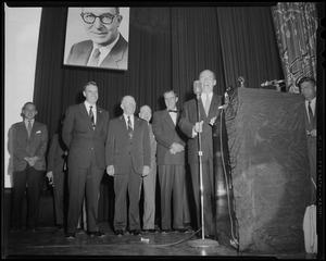 Adlai Stevenson standing at podium on stage with several others behind him