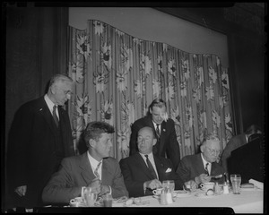 John F. Kennedy, Adlai Stevenson, and Mayor John B. Hynes seated at dinner table with Edward McCormack, (standing, right) and one other standing behind them