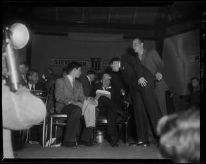 Adlai Stevenson seated on stage with hand on his head
