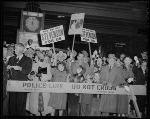 Crowd of Adlai Stevenson supporters behind a police barricade, holding signs
