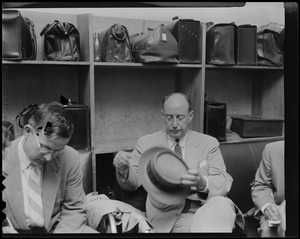 Adlai Stevenson sitting in luggage area and removing hat