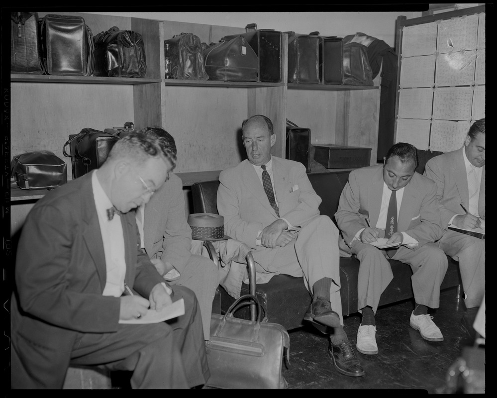 Adlai Stevenson, seated with others in a luggage area
