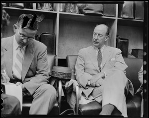 Adlai Stevenson seated and talking to another man in a luggage area