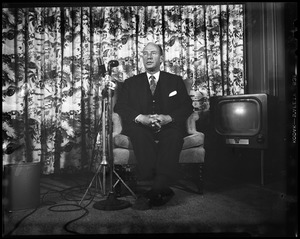 Adlai Stevenson sitting on a chair in front of a microphone