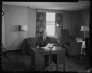 Adlai Stevenson sitting at a desk with microphone and paperwork