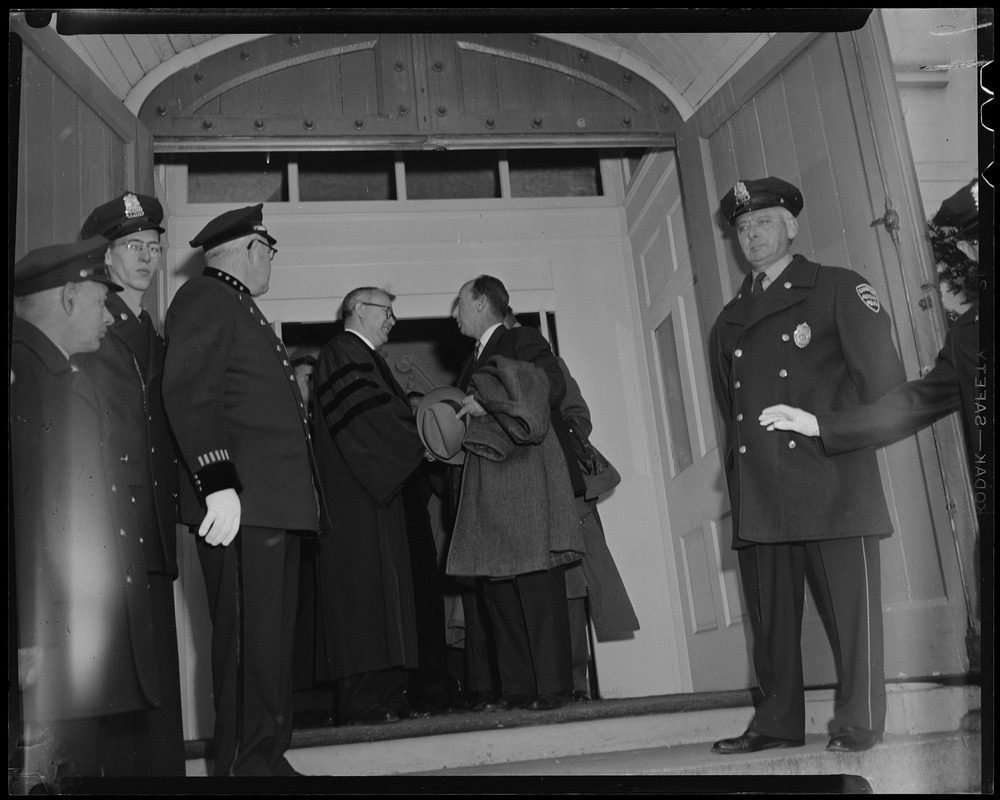 Adlai Stevenson speaking with a man in an academic robe in a doorway