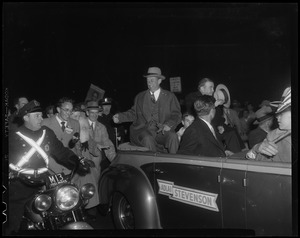 Adlai Stevenson sitting on the back of a car with a police officer beside them