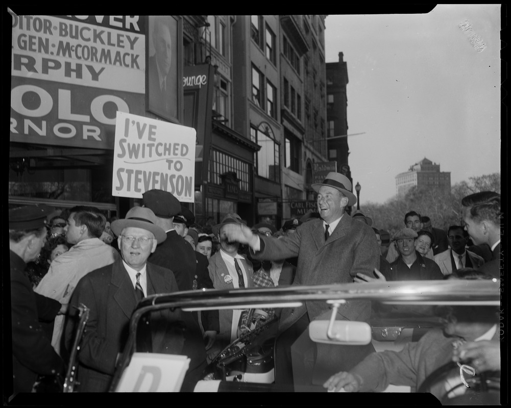 Adlai Stevenson sitting on the back of a car surrounded by a crowd