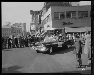 Adlai Stevenson sitting in a car with a crowd of people in the background