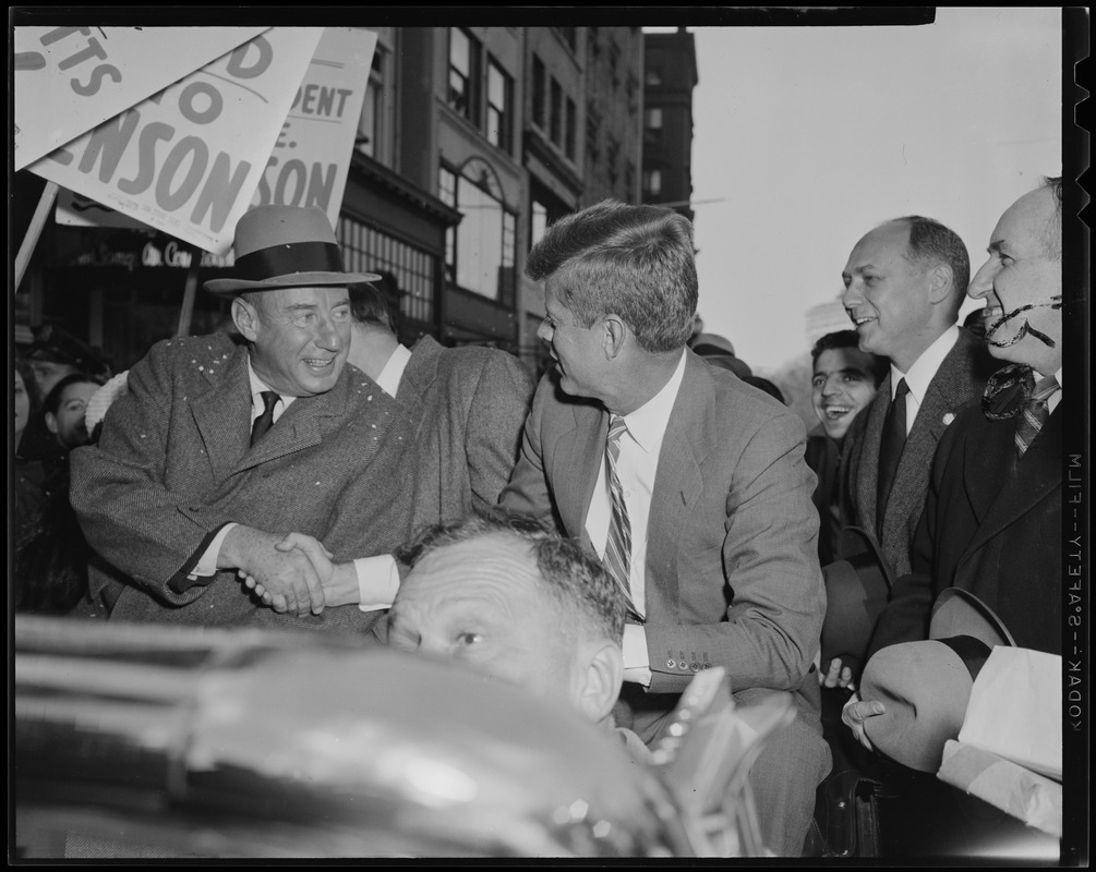 Adlai Stevenson and John F. Kennedy shaking hands in car during parade