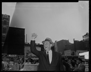 Adlai Stevenson waving with buildings seen in the background
