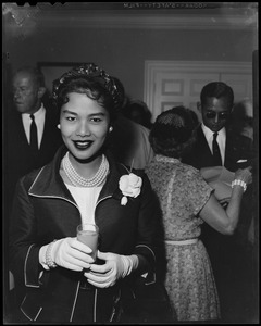 Queen Sirikit of Thailand holding a glass with people standing behind her