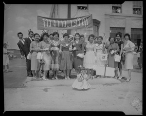 Group portrait of men, women and a young girl standing in front of a banner