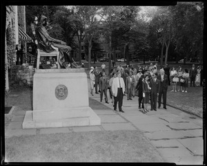 King Bhumibol Adulyadej and Queen Sirikit of Thailand walking with a group of people by statue of John Harvard in Harvard Yard