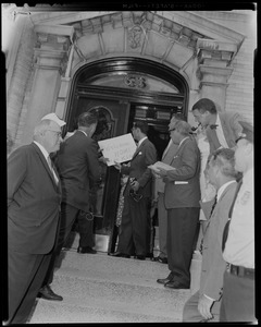 Group of men at entrance to a building, holding a "Welcome Home King" sign