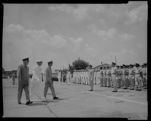 Groups of uniformed people standing at attention and saluting while King Bhumibol Adulyadej (right) and two others walk by