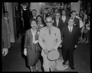 King Bhumibol Adulyadej and Queen Sirikit of Thailand entering a building, followed by a group of people