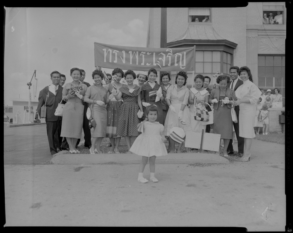 Group portrait of men, women and a young girl standing in front of a banner