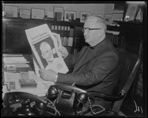 Clergyman sitting at desk with copy of the Record American Glenn Orbit Picture Book