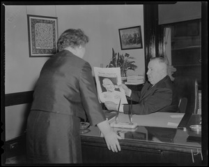Seated man showing a copy of the Record American Glenn Orbit Picture Book to a woman standing